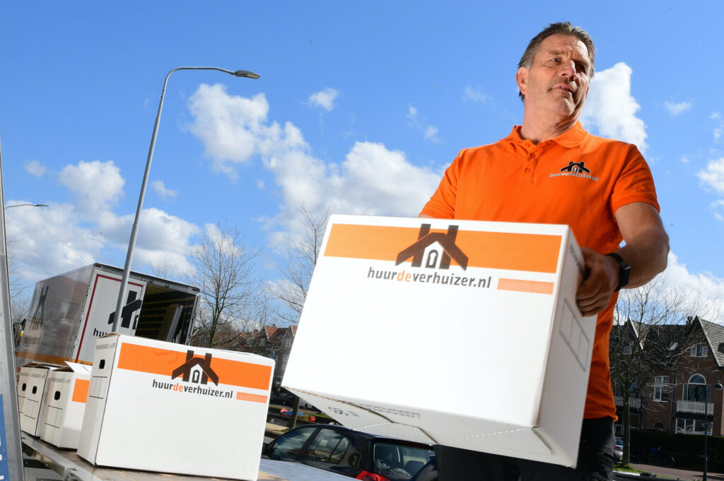 Verhuizer van Dekkers Verhuizingen tilt verhuisdoos naast verhuiswagen – werken in de buitenlucht met een enthousiast team